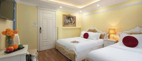 A hotel room with two beds, a desk with a vase of flowers, a painting on the wall, and a ceiling with recessed lighting.
