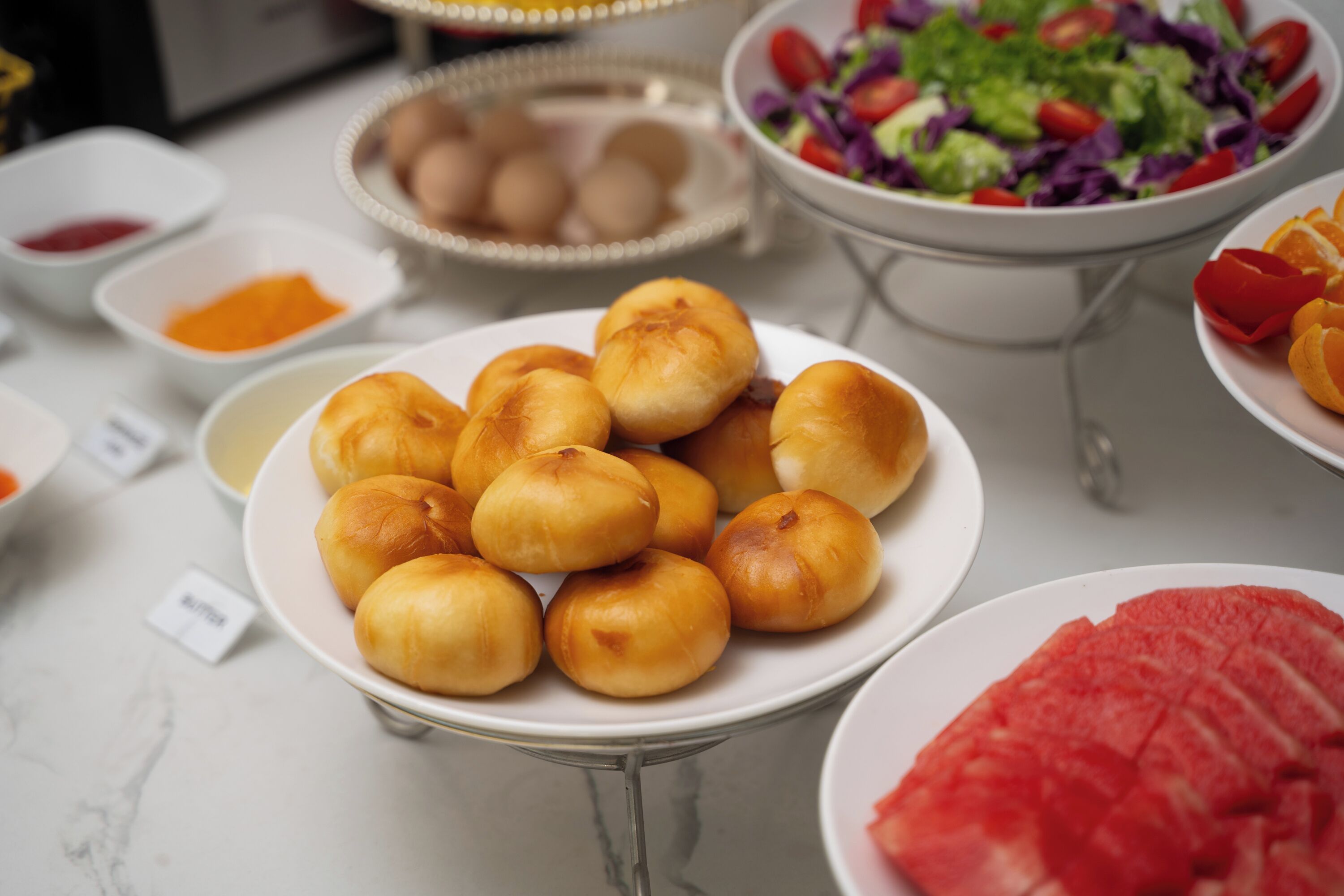 A buffet table with various dishes including rolls, a salad, and sliced meat.