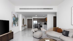 A modern living room with a flat-screen TV, a sofa, a coffee table, and a dining area in the background. - Maison Privee - Coastal Living w/ Uninterrupted Sea and Palm Views (Dubai)