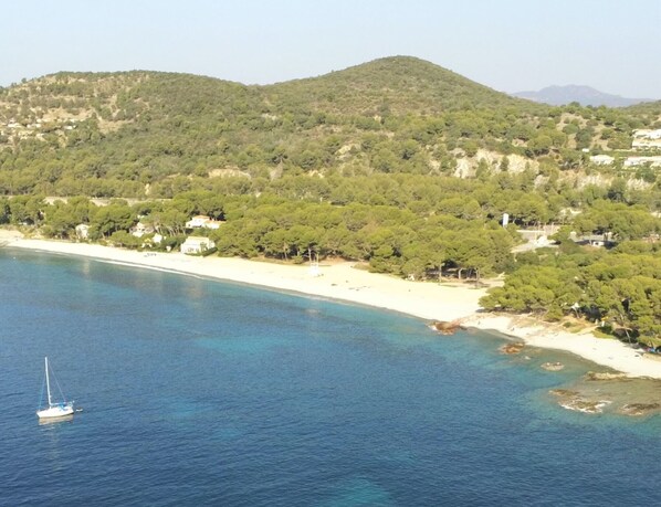 Zona costera con una playa arenosa, aguas azul cristalino y un velero.