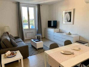 Una sala de estar moderna con un sofá, una mesa de centro, una mesa de comedor con posavasos con forma de pez, un televisor y una ventana con cortinas.