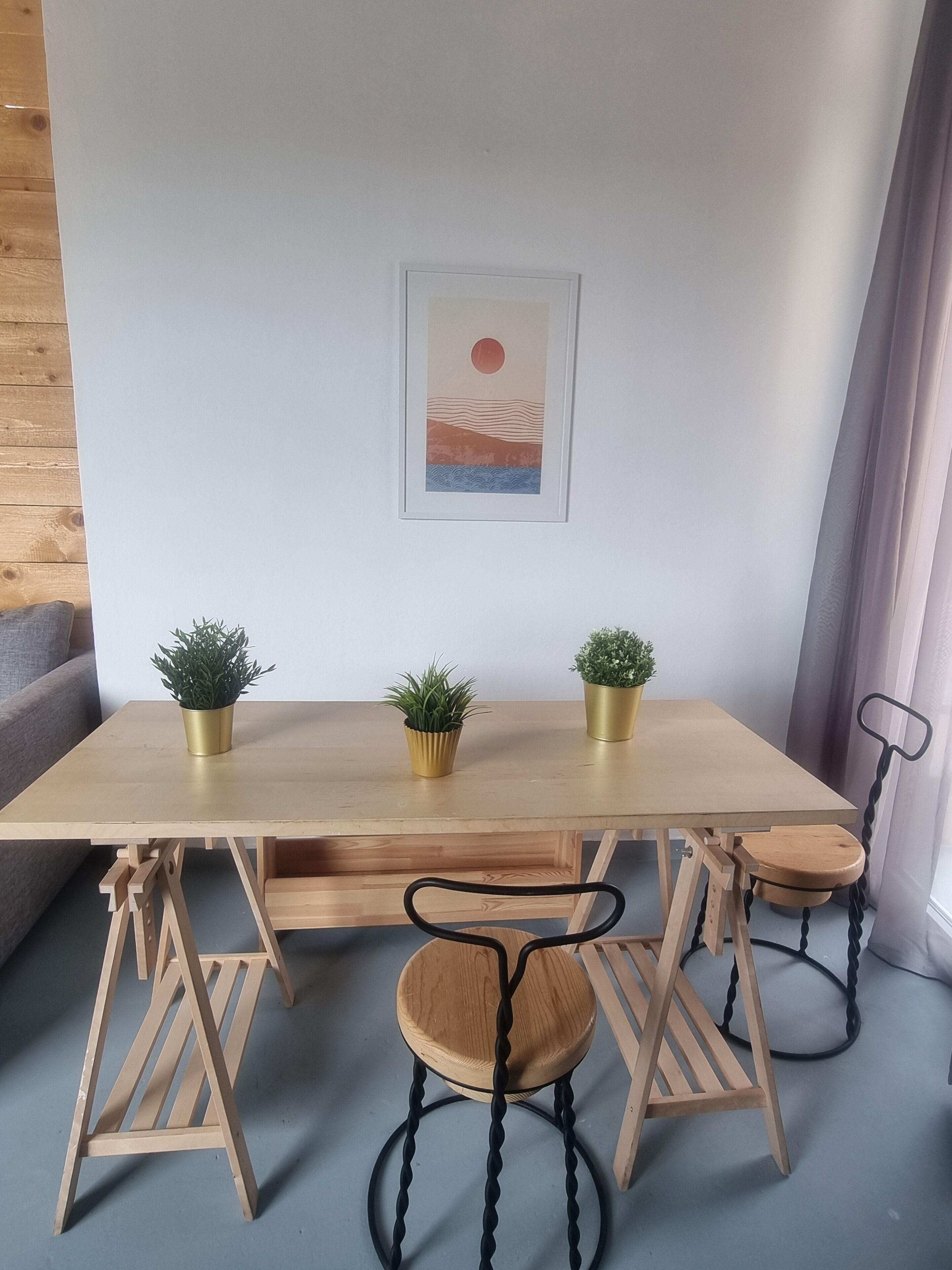 Una mesa de comedor de madera con tres sillas, cada una con una base negra en forma de espiral, y tres macetas con plantas en recipientes dorados.