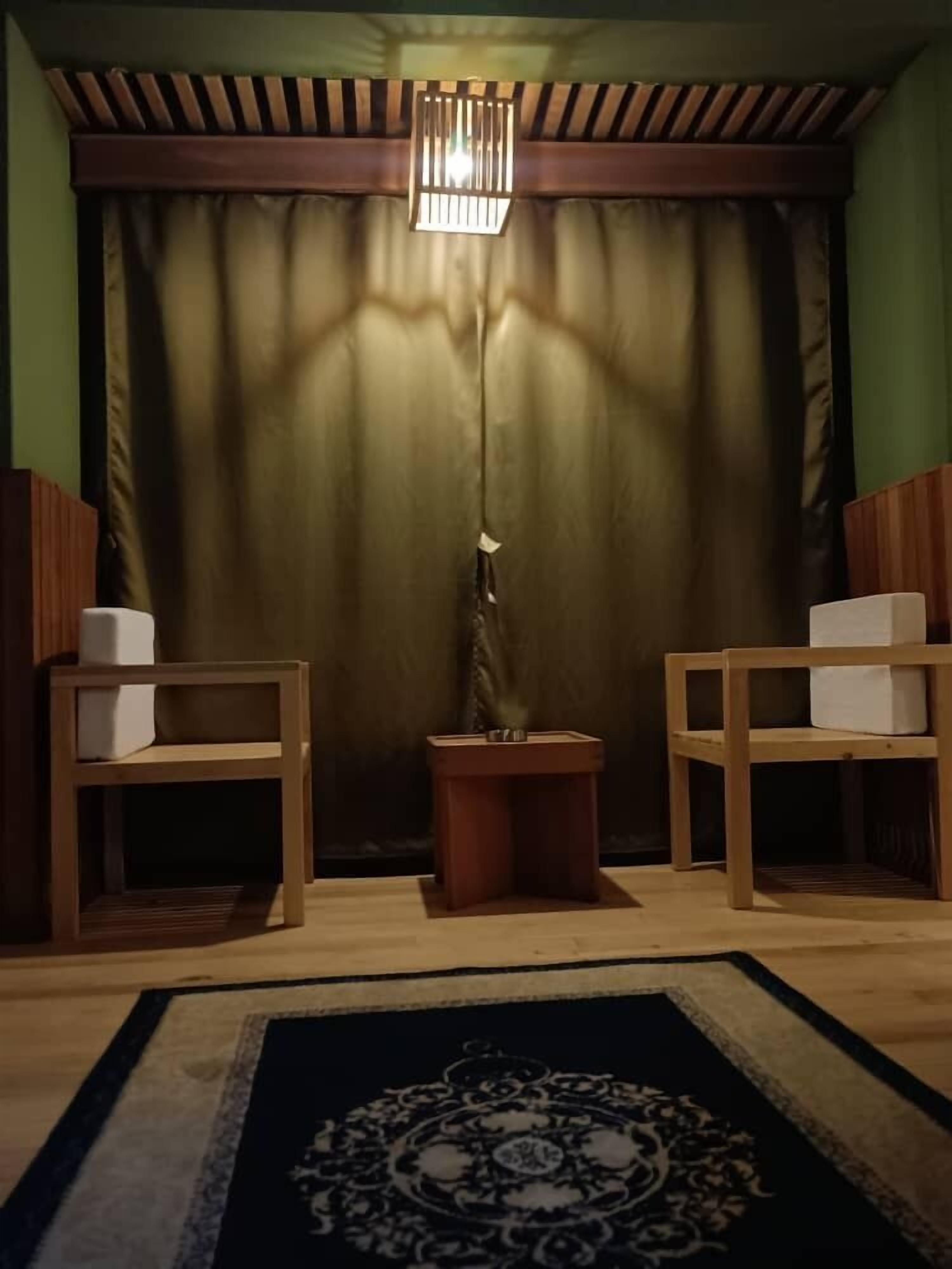 A room with a wooden ceiling, a central floor lamp, and two wooden side tables with boxes.