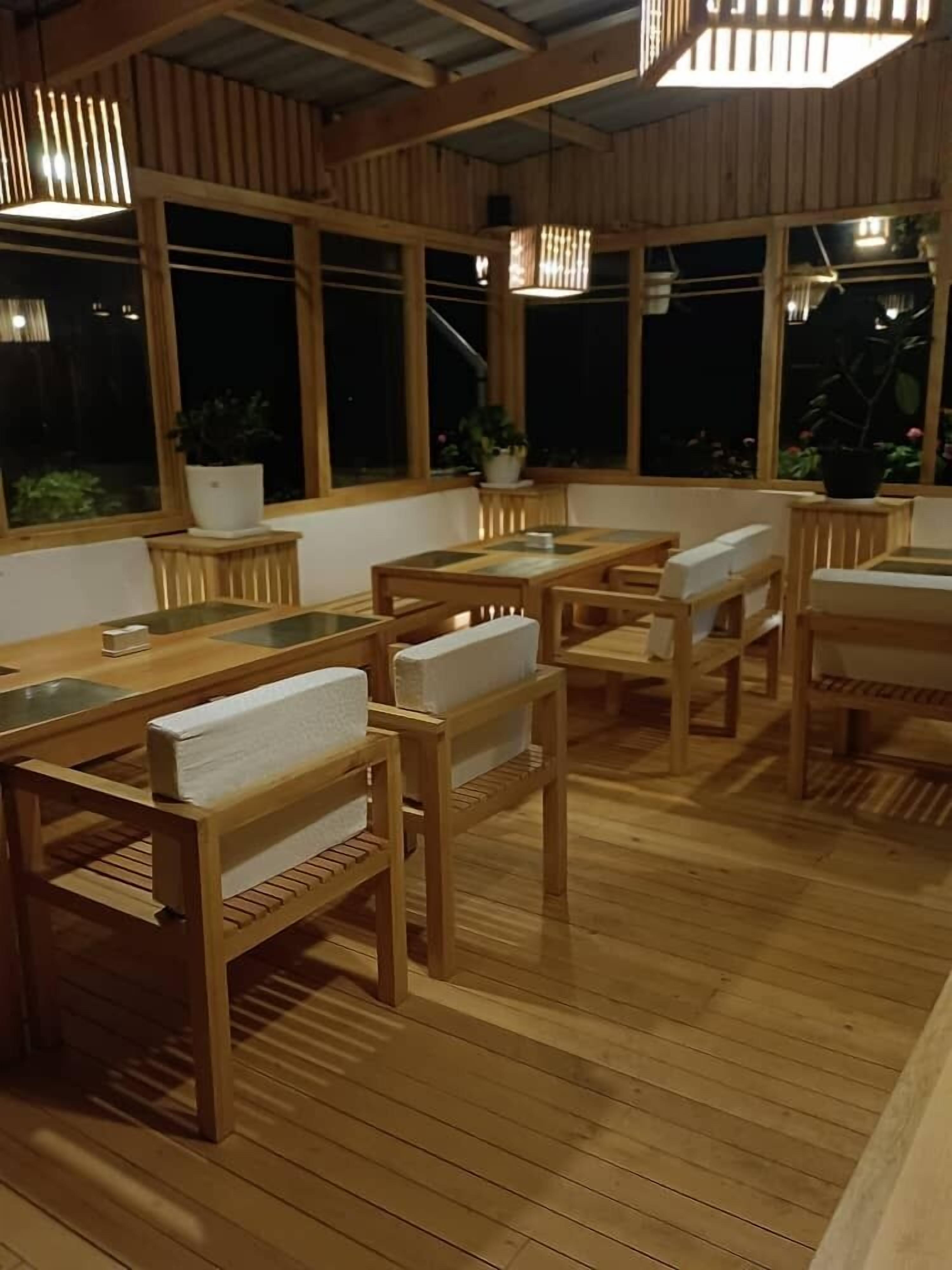 A wooden interior with tables and chairs, large windows, and potted plants.