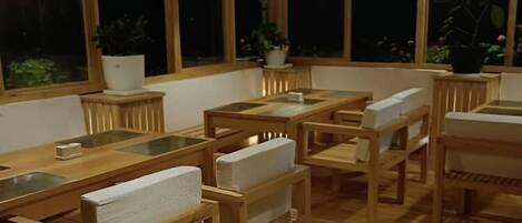A wooden interior with tables and chairs, large windows, and potted plants.