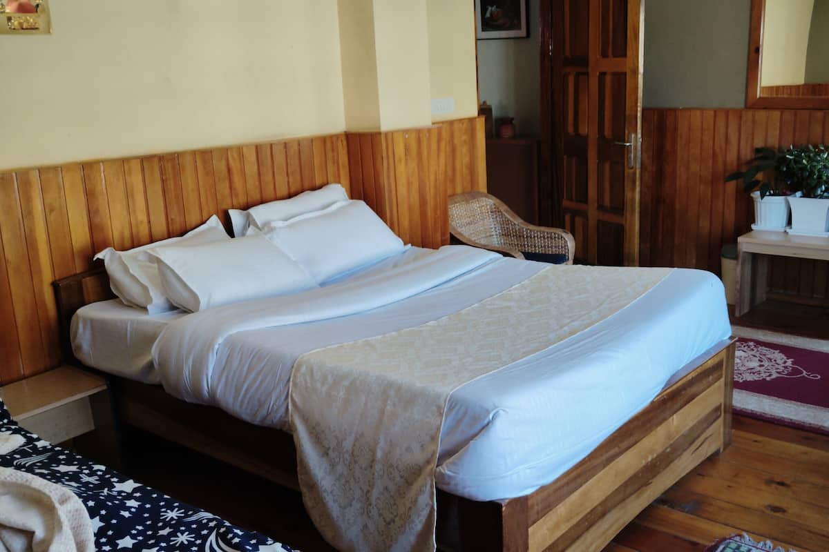 Ein Bett mit Holzbalken und weißen Leinentüchern, ein Korbstuhl, ein kleiner Tisch mit Topfpflanzen und ein Holzschrank.