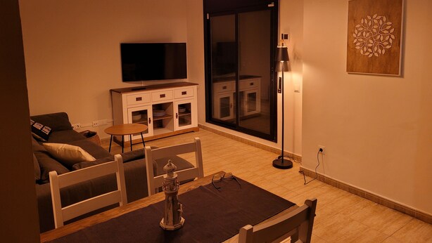 A living room with a flat-screen TV, a dining table with chairs, a sofa, a cabinet, and a floor lamp. - 5 minutes from the beach, bus terminal and nightlife! (Lloret de Mar)