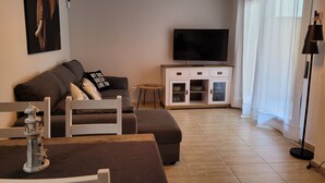 A modern living room with a sofa, a TV, a cabinet with glass doors, and a dining area with a table and chairs. - 5 minutes from the beach, bus terminal and nightlife! (Lloret de Mar)