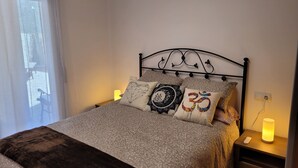 A neatly made bed with patterned bedding and decorative pillows, a bedside table with a lamp, and a power outlet on the wall. - 5 minutes from the beach, bus terminal and nightlife! (Lloret de Mar)