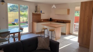 Une cuisine moderne dotée d’un îlot central, d’un coin repas avec une table en verre et d’un canapé agrémenté d’un coussin.