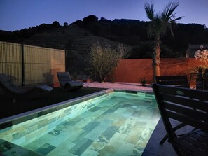Una piscina con solárium de baldosas, rodeada de sillas de descanso y una palmera.