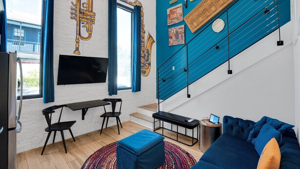A modern living room with a blue accent wall, a sofa, a coffee table, a TV, and a staircase.