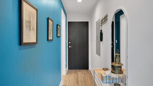 A hallway with blue walls, framed pictures, a door, and a display case with items.