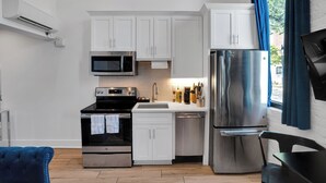 A modern kitchen with white cabinets, stainless steel appliances, and a blue chair.