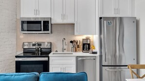 A compact kitchen with white cabinets, a stainless steel refrigerator, a microwave, a stove, and a coffee maker. - Frenchmen St Gem • Walk to French Quarter (New Orleans)