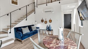 Un salon moderne avec un canapé bleu, une table ronde en marbre et un escalier doté d’une rampe noire.