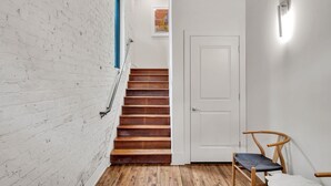 Una escalera con peldaños de madera que conduce a una puerta blanca, una pared de ladrillo blanco y un suelo de madera.