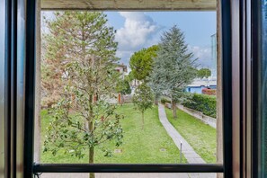 A view through a window of a grassy outdoor area with trees and a pathway. - Flower 41 - with patio and air conditioning (Sirmione)