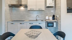 A compact kitchen with a modern design, featuring light-colored cabinets, a stainless steel range hood, a built-in microwave, and a small countertop with a kettle and coffee maker.
