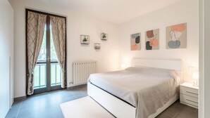 Un dormitorio con cama, ventana con cortinas, radiador y decoración en la pared.