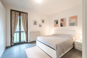 Un dormitorio con cama, ventana con cortinas, radiador y decoración en la pared.