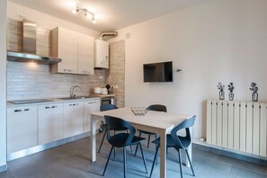 A modern kitchen with white cabinets, a stainless steel range hood, and a built-in oven. There is a dining table with four chairs and a flat-screen TV mounted on the wall. - Flower 41 - with patio and air conditioning (Sirmione)