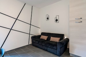 A modern living room with a black sofa, two cushions, a blue chair, and a white cabinet.