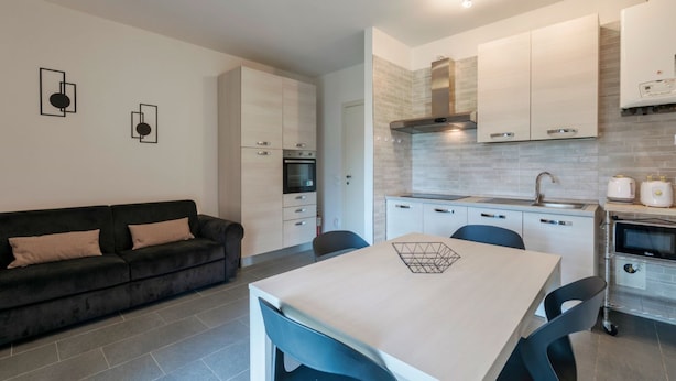 Una cocina moderna con armarios blancos, horno empotrado y comedor con mesa y sillas.
