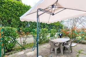 Un patio con mesa y sillas bajo una cubierta, rodeado de follaje y una cerca.
