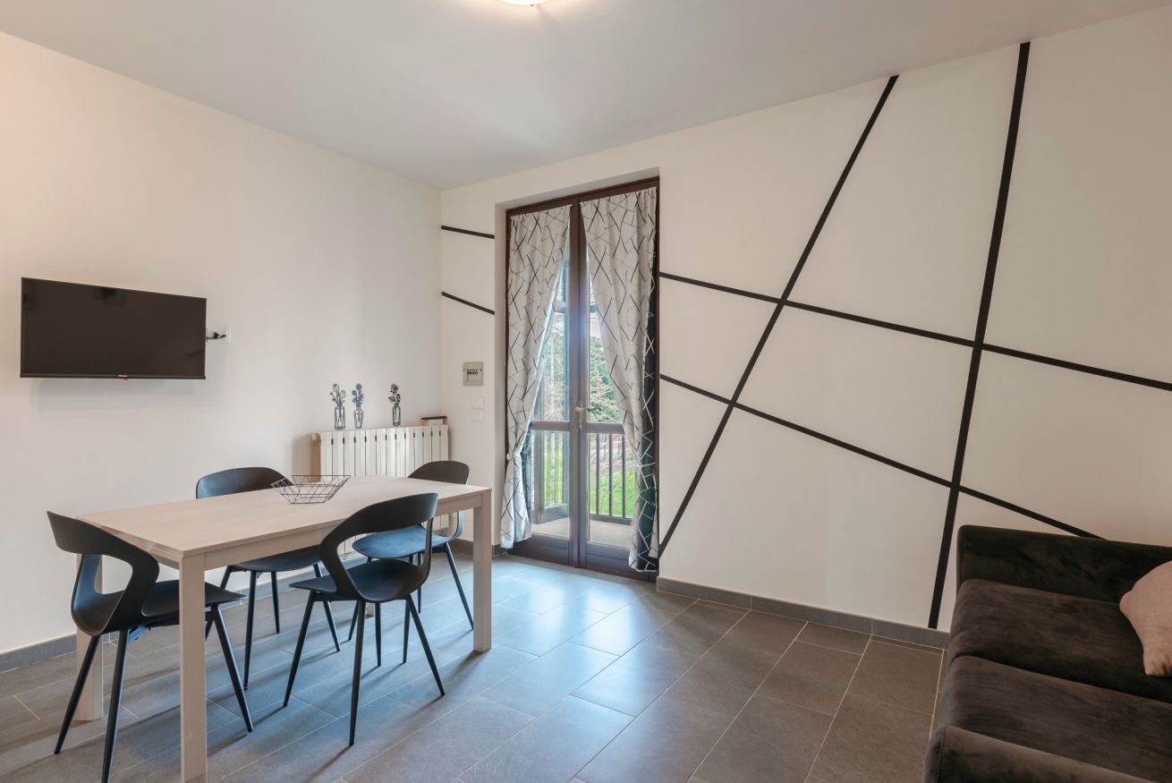 Een moderne eetruimte met een tafel en stoelen, een aan de muur bevestigde televisie en een schuifdeur naar een balkon.