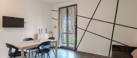 Een moderne eetruimte met een tafel en stoelen, een aan de muur bevestigde televisie en een schuifdeur naar een balkon.
