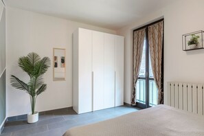A bedroom with a bed, a wardrobe, a potted plant, a radiator, and a window with curtains. - Flower 41 - with patio and air conditioning (Sirmione)