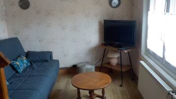 A living room with a blue sofa, a wooden coffee table, a television on a stand, and two wall clocks.
