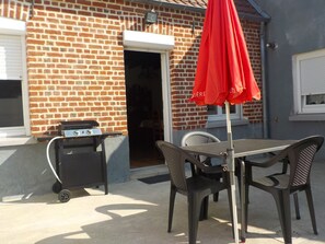 A patio with a grill, outdoor table, and chairs.