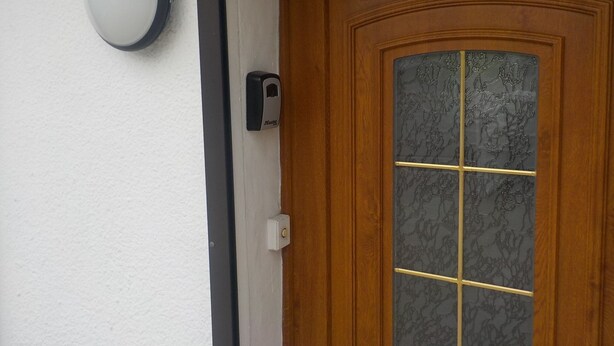 Eine Holztür mit Fensterglas, Klingel und einem an der Wand montierten Gegensprechanlage.