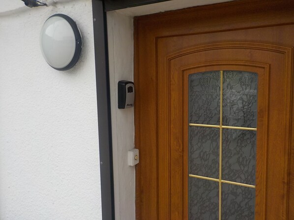 A wooden door with a glass panel, a doorbell, and a wall-mounted intercom.