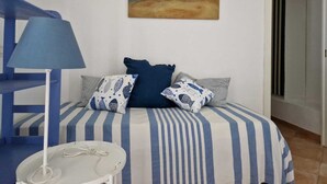 Un dormitorio con una colcha a rayas, una lámpara azul y un cuadro de una playa.