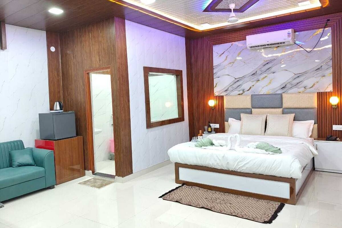 Une chambre moderne avec un grand lit, un canapé, une télévision et un mur décoré d’un motif imitant le marbre.