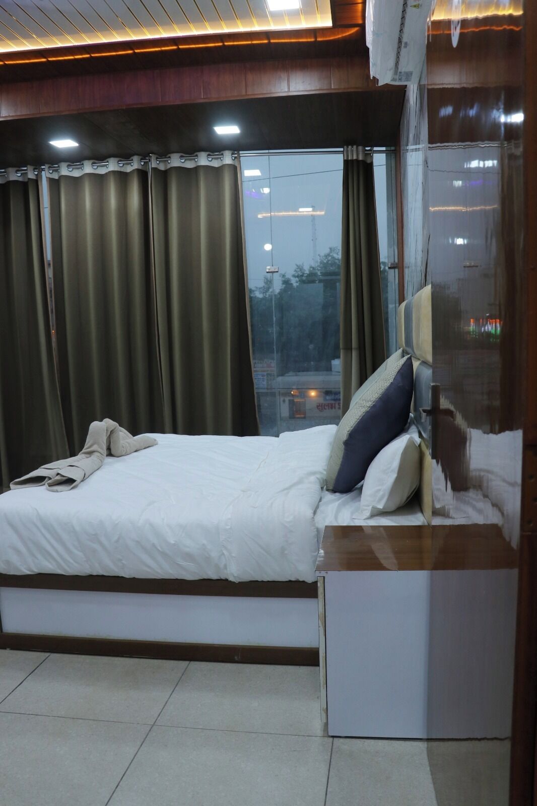 Habitación de hotel con cama, mesita de noche, ventana con cortinas y vistas al exterior.