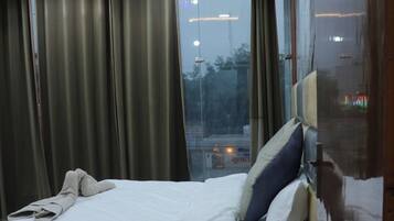 Habitación de hotel con cama, mesita de noche, ventana con cortinas y vistas al exterior.