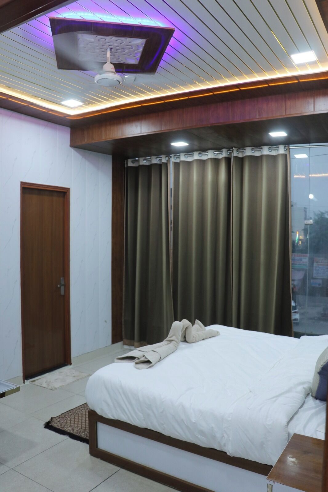 A bedroom with a bed, curtains, a ceiling fan, and a window with a view.