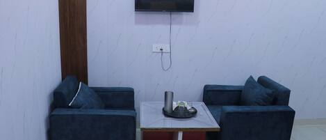 A room with two dark blue sofas, a small table with a tray, a television mounted on the wall, and a wooden door.