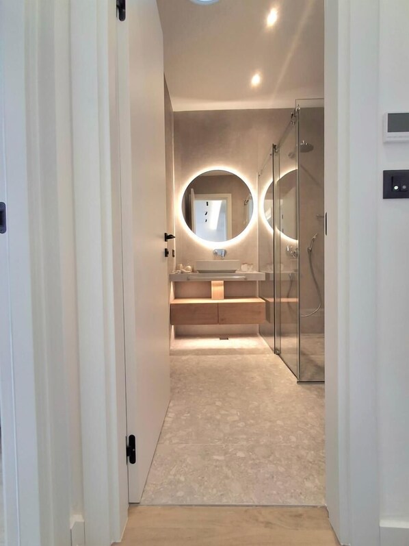 A modern bathroom with a round mirror, a glass shower enclosure, and a beige tiled floor.