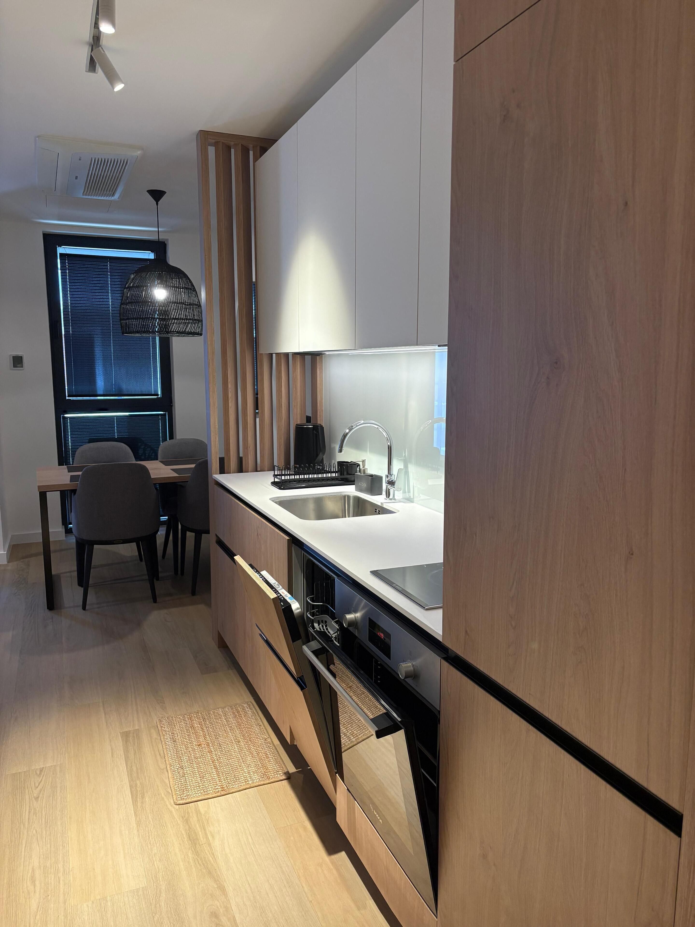 A modern kitchen with a built-in oven, a sink, and a dining area with a table and chairs.