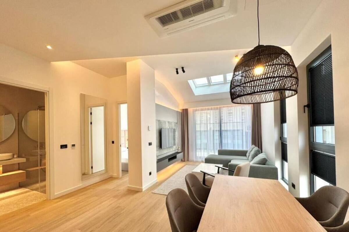 A modern living room with a dining area, a staircase, and a large window with curtains.