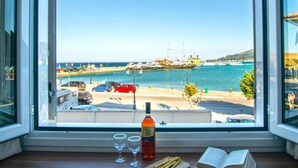 Blick aus dem Fenster auf einen Hafen mit Booten, einem roten Auto und einer Weinflasche auf einem Tisch.