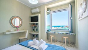 Ein Schlafzimmer mit einem Bett, einem Fenster mit Meerblick, einem Regal mit Fernseher und einem Sessel.