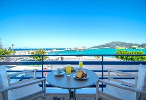 A balcony with a table set for breakfast, overlooking a coastal area with boats and a clear blue sky.
