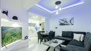 Un salon moderne avec une table basse en verre, un canapé foncé et un téléviseur à écran plat fixé au mur.
