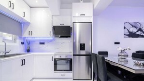 Une cuisine moderne avec des meubles blancs, un réfrigérateur en acier inoxydable, un four et un coin repas comprenant une table et des chaises.